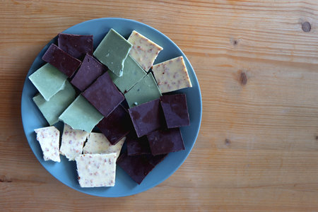 Plate with dark, white and matcha chocolate pieces. Top view, wooden background.の写真素材