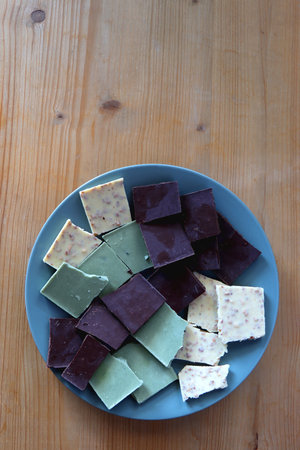 Plate with dark, white and matcha chocolate pieces. Top view, wooden background.の写真素材