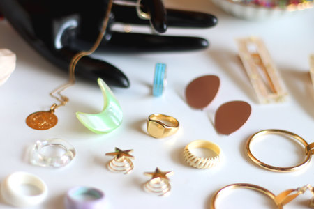 Hand figurine, sunglasses, gold jewelry, colorful bead jewelry, statement rings and various hair accessories on the white table. Selective focus.の写真素材
