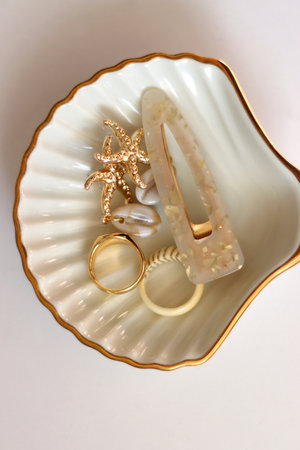 White shell shaped trinket with gold and beige accessories. Top view, white background.の写真素材