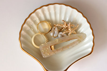 White shell shaped trinket with gold and beige accessories. Top view, white background.の写真素材