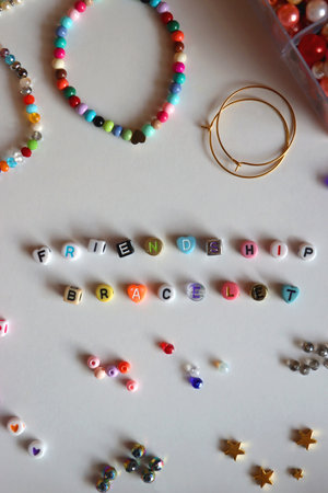 Friendship bracelet spelled with letter beads. Colorful handmade bracelets and various jewelry making supplies. Top view, white background.の写真素材