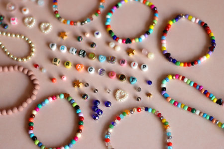 Friendship bracelet spelled with letter beads. Colorful handmade bracelets and various beads. Selective focus, pink background.の写真素材