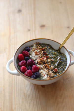 Beige bowl with green smoothie, frozen berries and homemade granola, served on the table. Selective focus.の写真素材