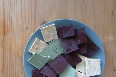 Plate with dark, white and matcha chocolate pieces. Top view, wooden background.の写真素材