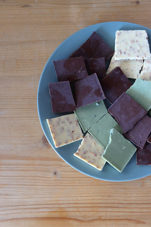 Plate with dark, white and matcha chocolate pieces. Top view, wooden background.の写真素材