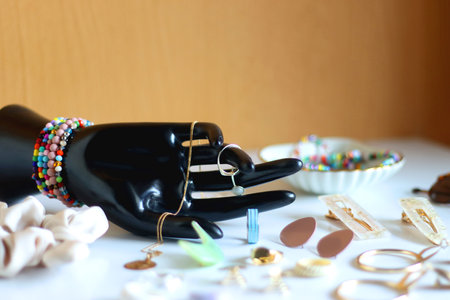 Hand figurine, sunglasses, gold jewelry, colorful bead jewelry, statement rings and various hair accessories on the white table. Selective focus.の写真素材