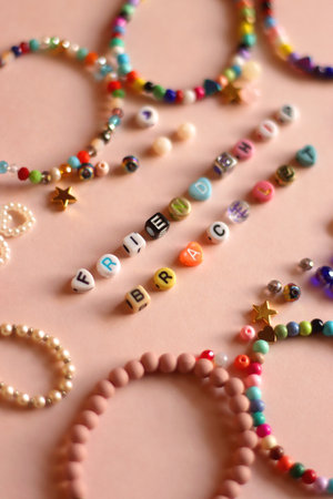 Friendship bracelet spelled with letter beads. Colorful handmade bracelets and various beads. Selective focus, pink background.の写真素材