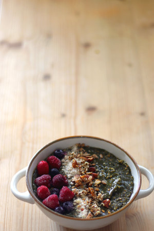 Beige bowl with green smoothie, frozen berries and homemade granola, served on the table. Selective focus.の写真素材
