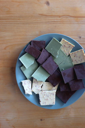 Plate with dark, white and matcha chocolate pieces. Top view, wooden background.の写真素材