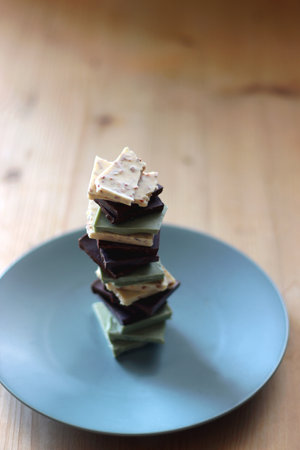 Pile of various chocolate pieces on a plate. Dark, white and matcha chocolate. Selective focus.の写真素材