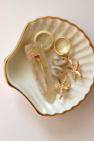 White shell shaped trinket with gold and beige accessories. Top view, white background.の写真素材