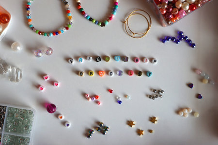 Friendship bracelet spelled with letter beads. Colorful handmade bracelets and various jewelry making supplies. Top view, white background.の写真素材
