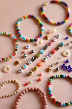 Friendship bracelet spelled with letter beads. Colorful handmade bracelets and various beads. Selective focus, pink background.の写真素材