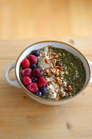 Beige bowl with green smoothie, frozen berries and homemade granola, served on the table. Selective focus.の写真素材