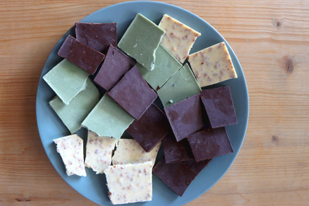 Plate with dark, white and matcha chocolate pieces. Top view, wooden background.の写真素材