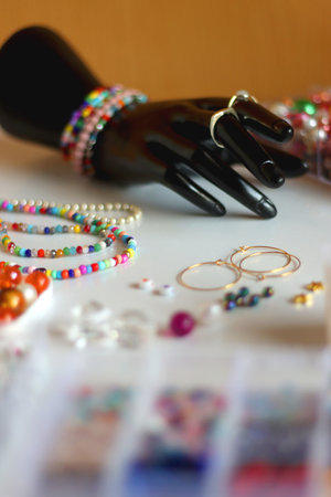 Hand figurine, colorful friendship bracelets, necklaces, various beads and DIY supplies on the table. Making jewelry at home. Selective focus.の写真素材