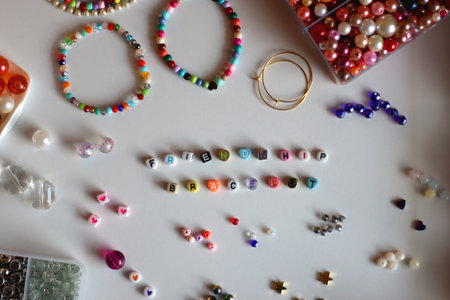 Friendship bracelet spelled with letter beads. Colorful handmade bracelets and various jewelry making supplies. Top view, white background.の写真素材