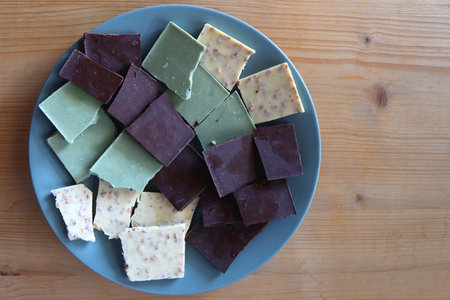 Plate with dark, white and matcha chocolate pieces. Top view, wooden background.の写真素材