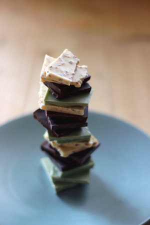 Pile of various chocolate pieces on a plate. Dark, white and matcha chocolate. Selective focus.の写真素材