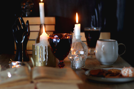 Books, lit candles, red wine, snacks and various decoration on the table. Dark academia or Halloween concept. Selective focus.の写真素材