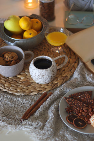 Books, e-reader, tea, orange juice, fruit, snacks, yarn, blanket and lit candles on the table. Autumn or winter hygge at home. Selective focus.の写真素材