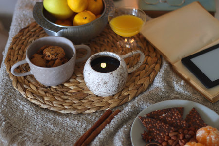 Books, e-reader, tea, orange juice, fruit, snacks, yarn, blanket and lit candles on the table. Autumn or winter hygge at home. Selective focus.の写真素材