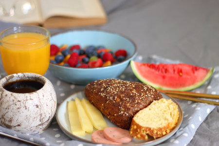 Tray with various healthy breakfast food, open book and reading glasses on the bed. Breakfast in bed concept. Selective focus.の写真素材