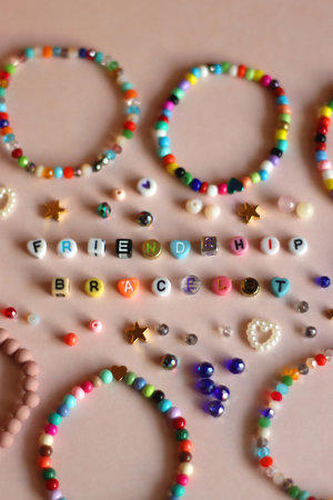 Friendship bracelet spelled with letter beads. Colorful handmade bracelets and various beads. Selective focus, pink background.の写真素材