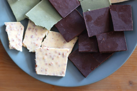 Plate with dark, white and matcha chocolate pieces. Top view, wooden background.の写真素材