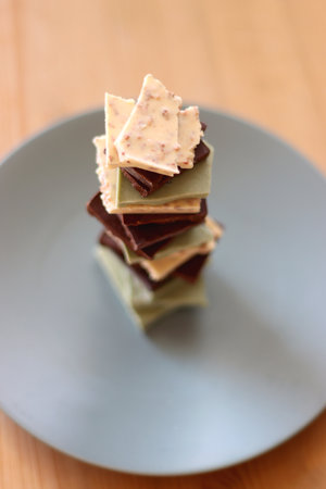 Pile of various chocolate pieces on a plate. Dark, white and matcha chocolate. Selective focus.の写真素材
