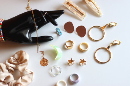 Hand figurine, sunglasses, gold jewelry, colorful bead jewelry, statement rings and various hair accessories on the white table. Selective focus.の写真素材