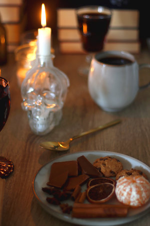 Books, lit candles, red wine, snacks and various decoration on the table. Dark academia or Halloween concept. Selective focus.の写真素材