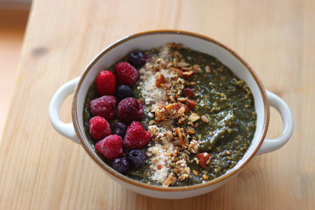 Beige bowl with green smoothie, frozen berries and homemade granola, served on the table. Selective focus.の写真素材