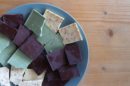 Plate with dark, white and matcha chocolate pieces. Top view, wooden background.の写真素材