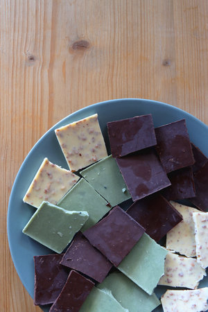 Plate with dark, white and matcha chocolate pieces. Top view, wooden background.の写真素材