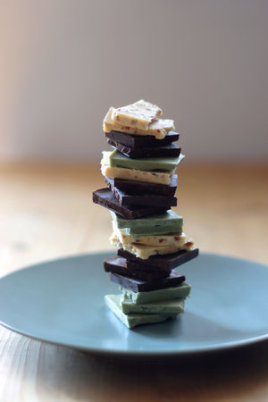 Pile of various chocolate pieces on a plate. Dark, white and matcha chocolate. Selective focus.の写真素材