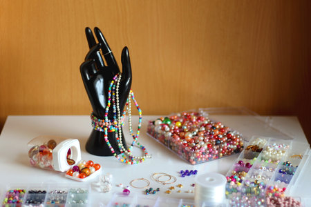 Hand figurine, colorful friendship bracelets, necklaces, various beads and DIY supplies on the table. Making jewelry at home. Selective focus.の写真素材