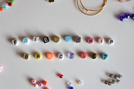 Friendship bracelet spelled with letter beads. Colorful handmade bracelets and various jewelry making supplies. Top view, white background.の写真素材