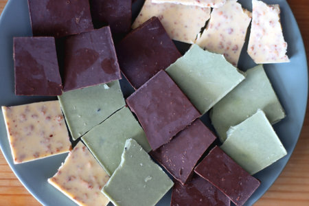 Plate with dark, white and matcha chocolate pieces. Top view, wooden background.の写真素材
