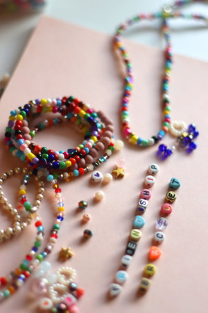 Friendship bracelet spelled with letter beads. Colorful handmade bracelets and various beads. Selective focus, pink background.の写真素材