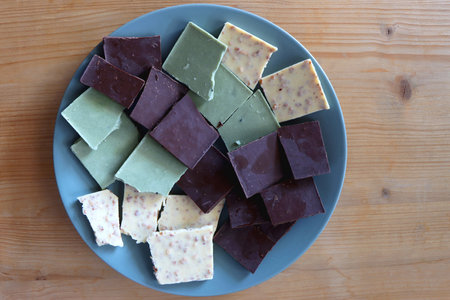 Plate with dark, white and matcha chocolate pieces. Top view, wooden background.の写真素材