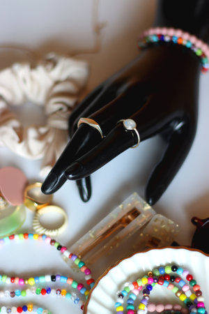 Hand figurine, sunglasses, gold jewelry, colorful bead jewelry, statement rings and various hair accessories on the white table. Selective focus.の写真素材