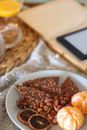 Books, tablet, orange juice, fruit, snacks, blanket and lit candles on the table. Autumn or winter hygge at home. Selective focus.の写真素材