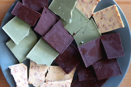 Plate with dark, white and matcha chocolate pieces. Top view, wooden background.の写真素材