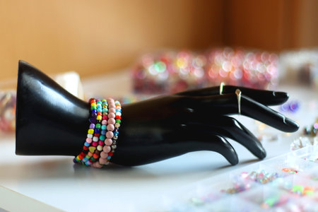 Hand figurine, colorful friendship bracelets, necklaces, various beads and DIY supplies on the table. Making jewelry at home. Selective focus.の写真素材