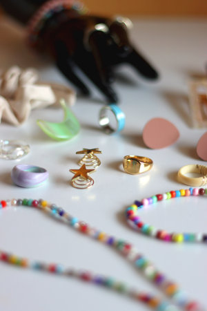 Hand figurine, gold jewelry, colorful bead jewelry, statement rings and various hair accessories on the white table. Selective focus.の写真素材
