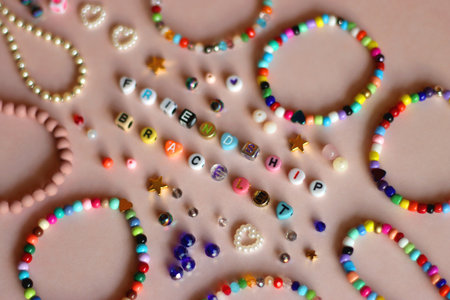Friendship bracelet spelled with letter beads. Colorful handmade bracelets and various beads. Selective focus, pink background.の写真素材