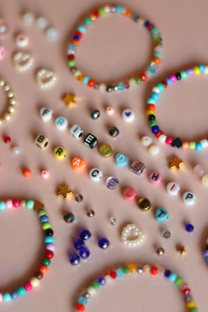 Friendship bracelet spelled with letter beads. Colorful handmade bracelets and various beads. Selective focus, pink background.の写真素材
