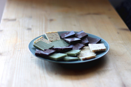 Plate with dark, white and matcha chocolate pieces. Selective focus, wooden background.の写真素材